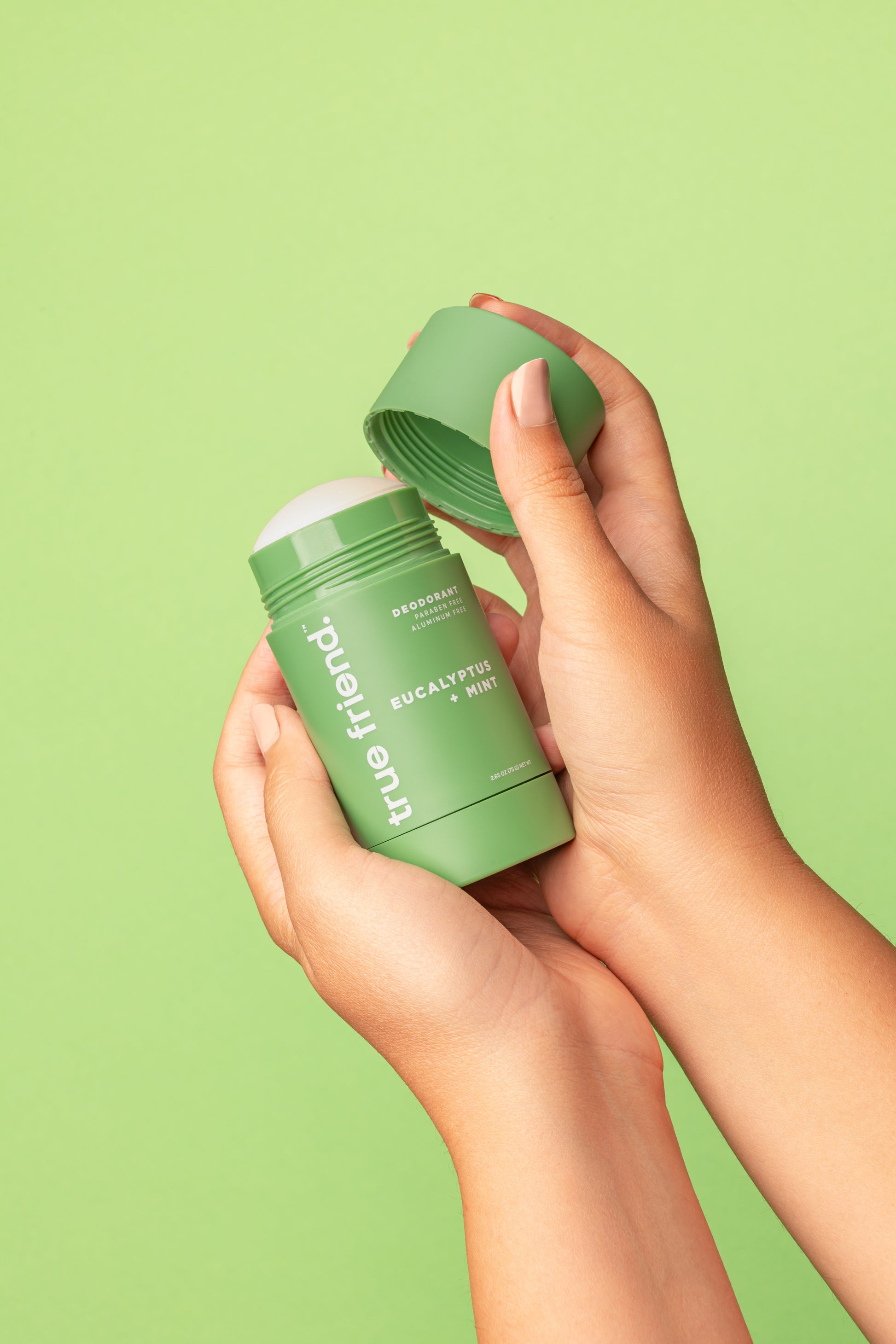 Hand holding a green eucalyptus + mint deodorant stick with 'true friend' branding against a green background