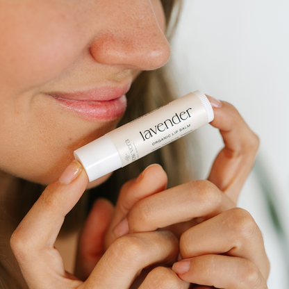 Woman applying lavender lip balm to her lips with a blurred background