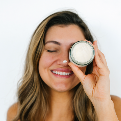 Woman applying tallow cream to her face with a white background.
