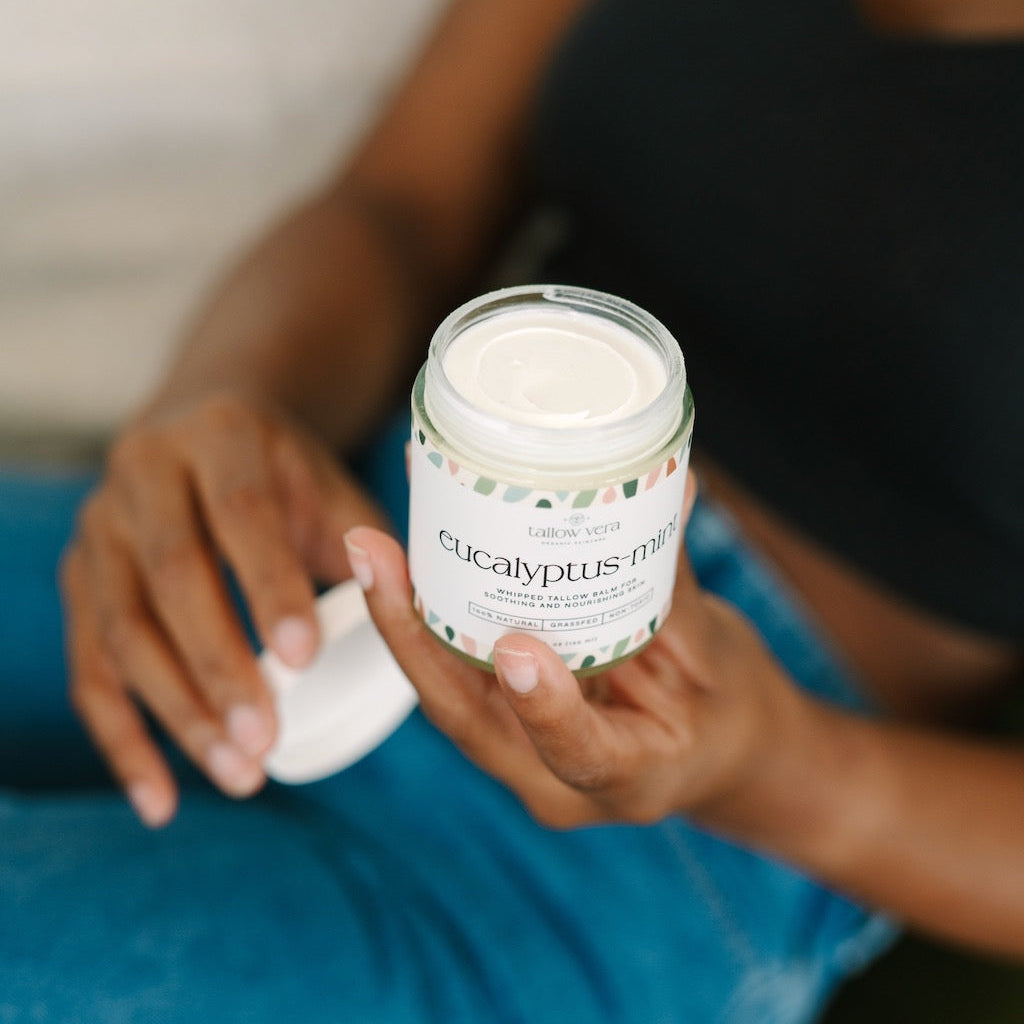 Girl holding a jar of 'eucalyptus-mint' Tallow Vera tallow balm with a blurred background