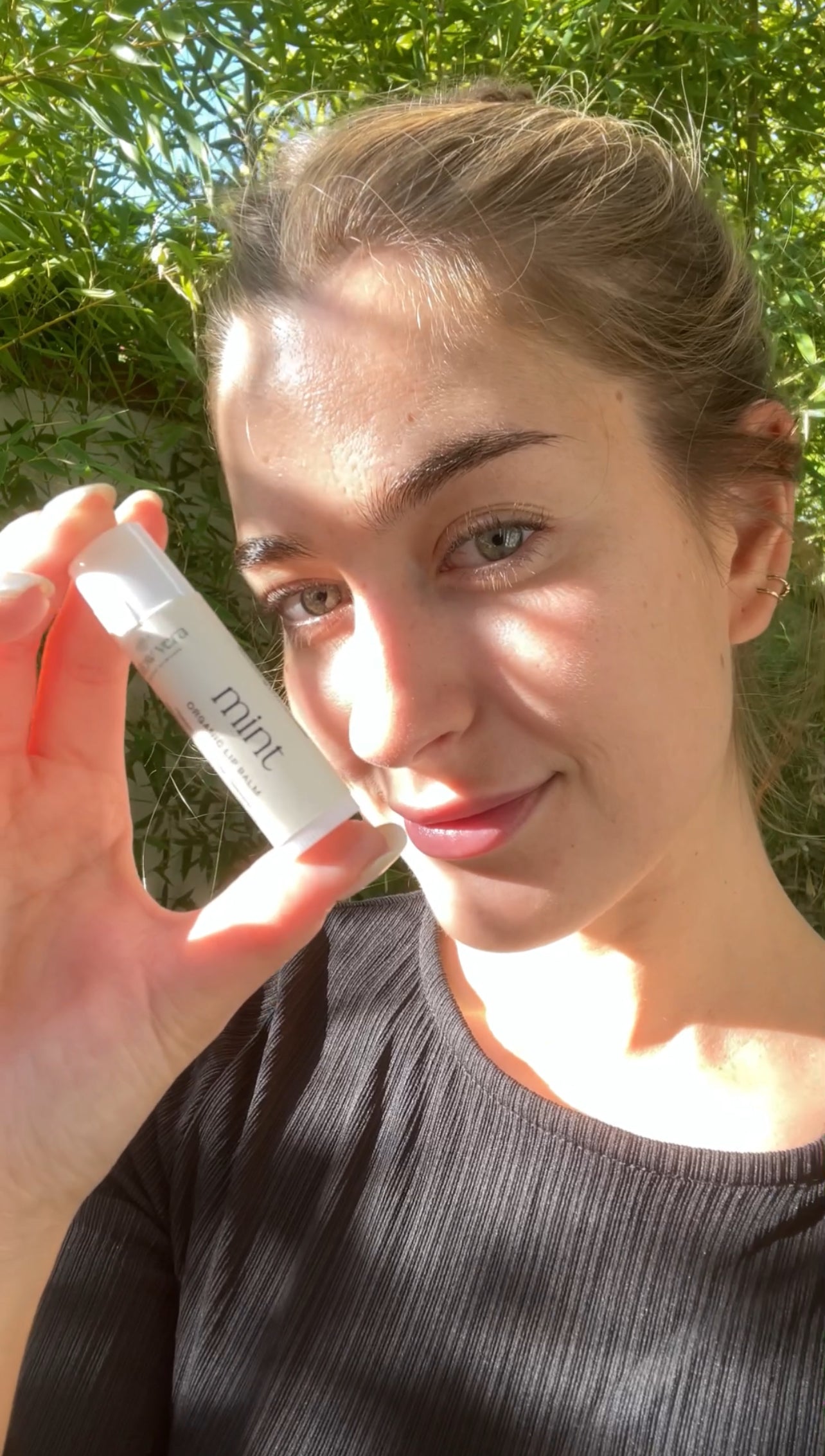 Woman holding Tallow Vera's mint tallow lip balm white with a green outdoor background.