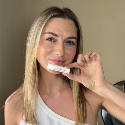woman holding a lavender tallow vera lip balm by her lips