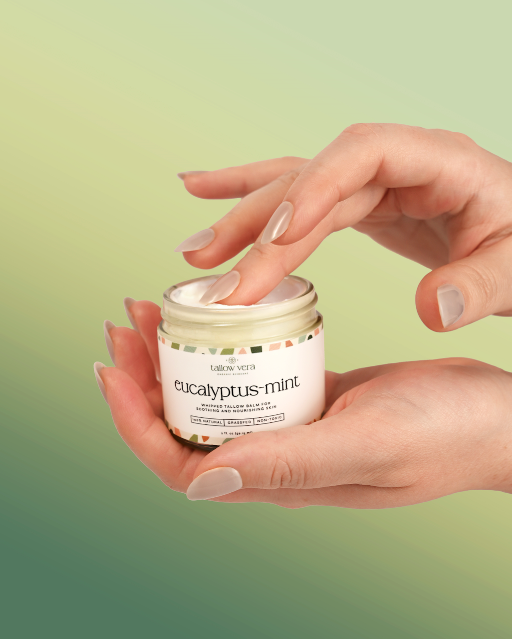 Hand holding a jar of Tallow Vera eucalyptus-mint tallow cream against a green gradient background
